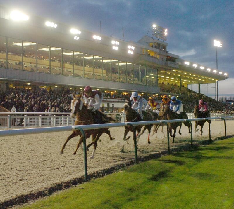 Horses race round the first bend at Wolverhampton Racecourse in front of a packed grandstand at night time