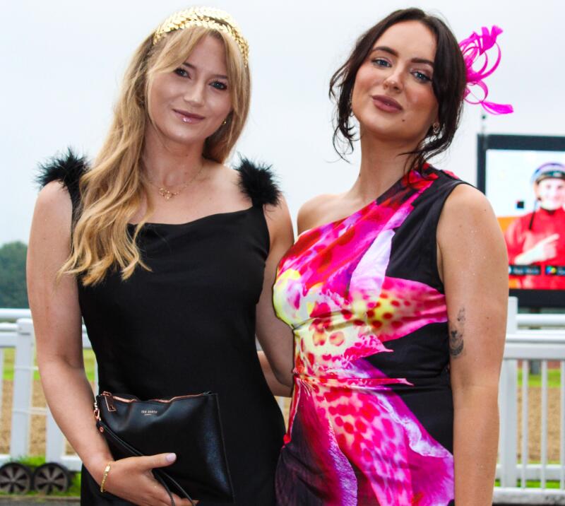 Two young women, one on the left in a black dress and the one on the right in a colourful pink dress
