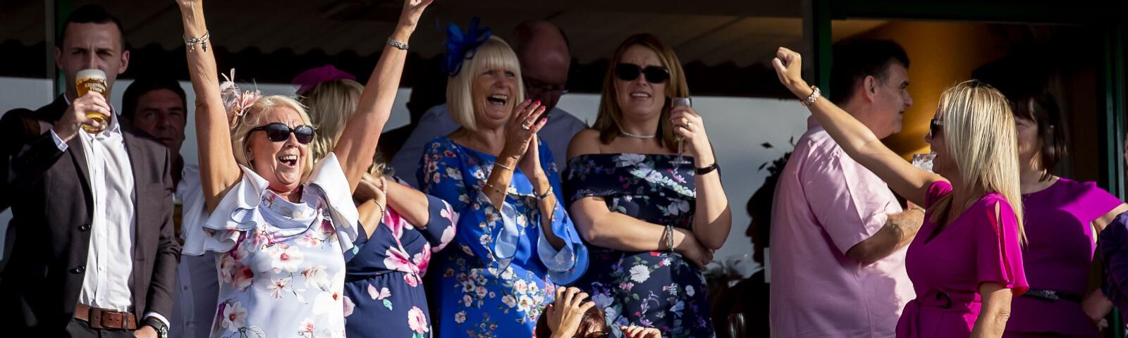 A group of well dressed hospitality guests at Wolverhampton Races celebrate a race.