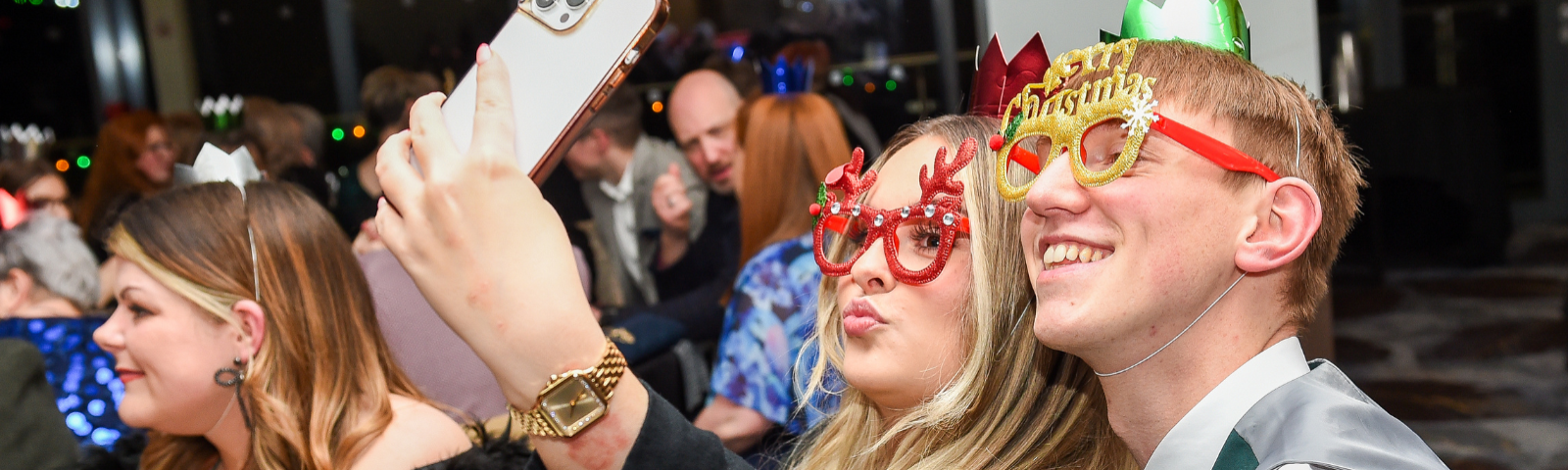 Two young people smiling and posing for a photo with festive accessories on.
